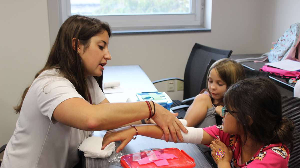 Nursing student shows girl scouts how to wrap an arm.