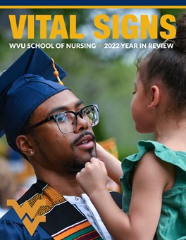 A young black man with dark rimmed glasses is seen wearing graduation regalia and holding a young child in his arms. Above him is the text, “Vital Signs: WVU School of Nursing, 2022 Year in Review.” In the bottom left corner is the gold Flying WV logo.