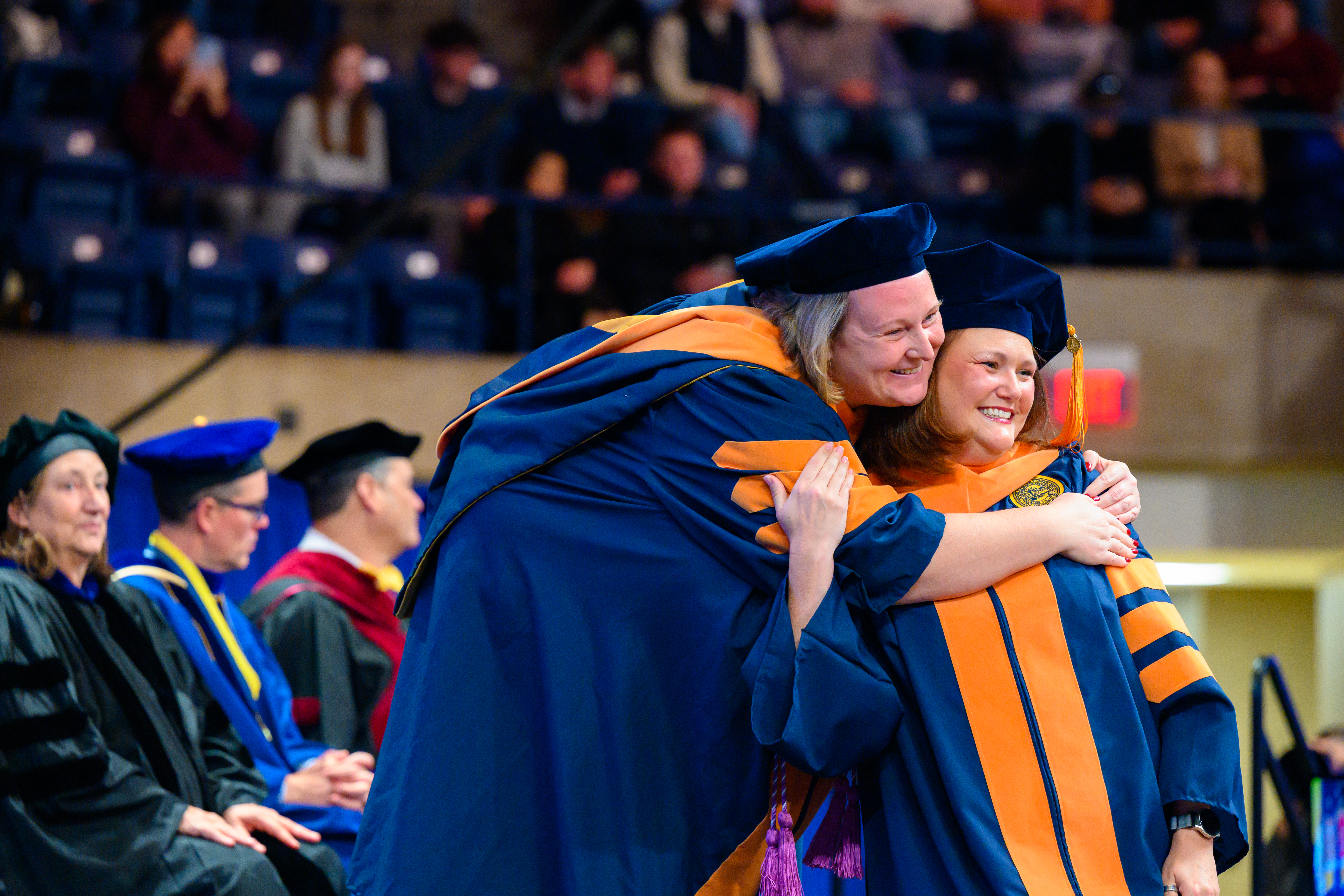 A nursing faculty member hugs a nursing student on stage at graduation.