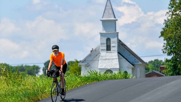 A cyclist rides on a quiet country road near a quiet country church.