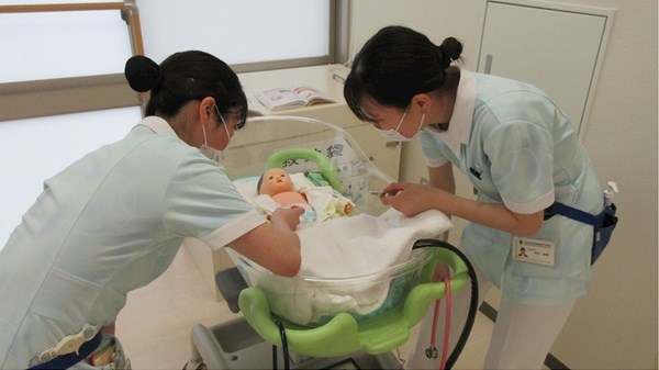 Two nursing students in Japan work with an infant manikin.