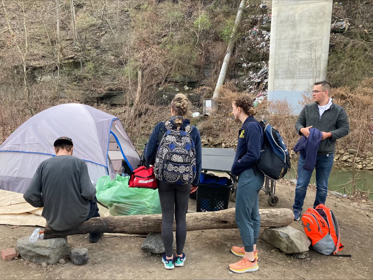 Student teams work outdoors with an individual experiencing homelessness outside of a tent.