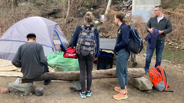 Student teams work outdoors with an individual experiencing homelessness outside of a tent.