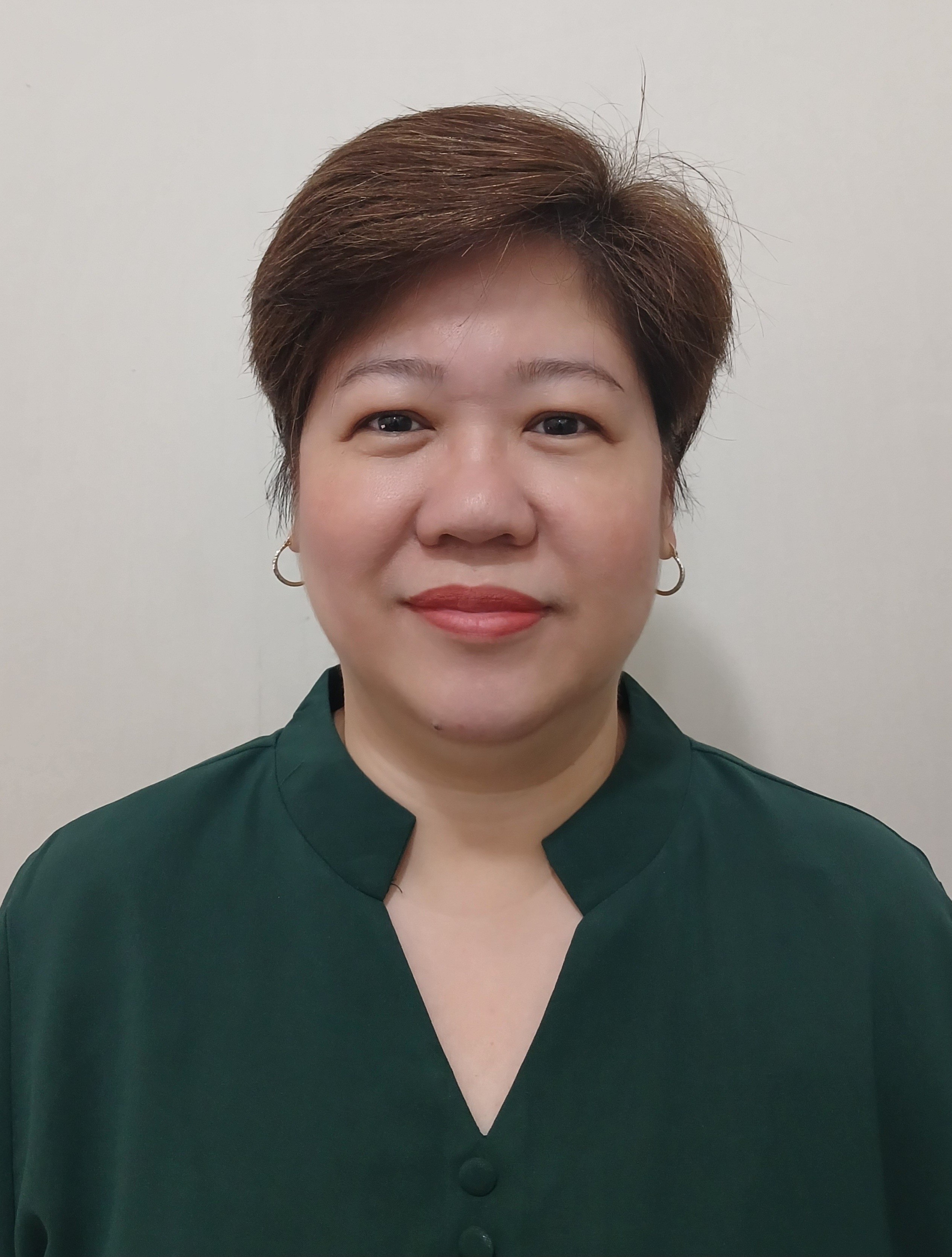 Emerita poses, smiling for the camera, while standing in front of an off-white backdrop.