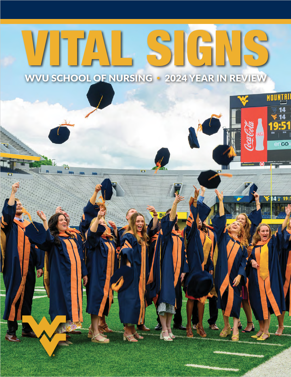 A group of graduates in full commencement regalia standing on Mountaineer Field toss their caps in the air.